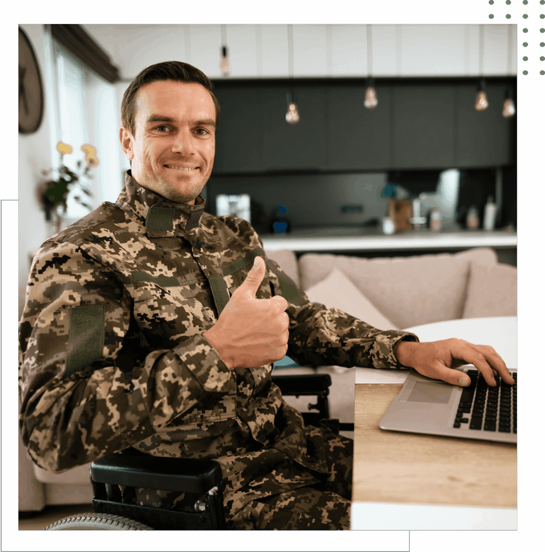 Man in camouflage, thumbs up, using laptop.