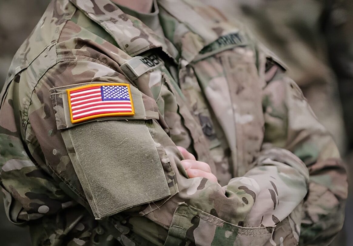 Soldier in camouflage uniform with American flag.